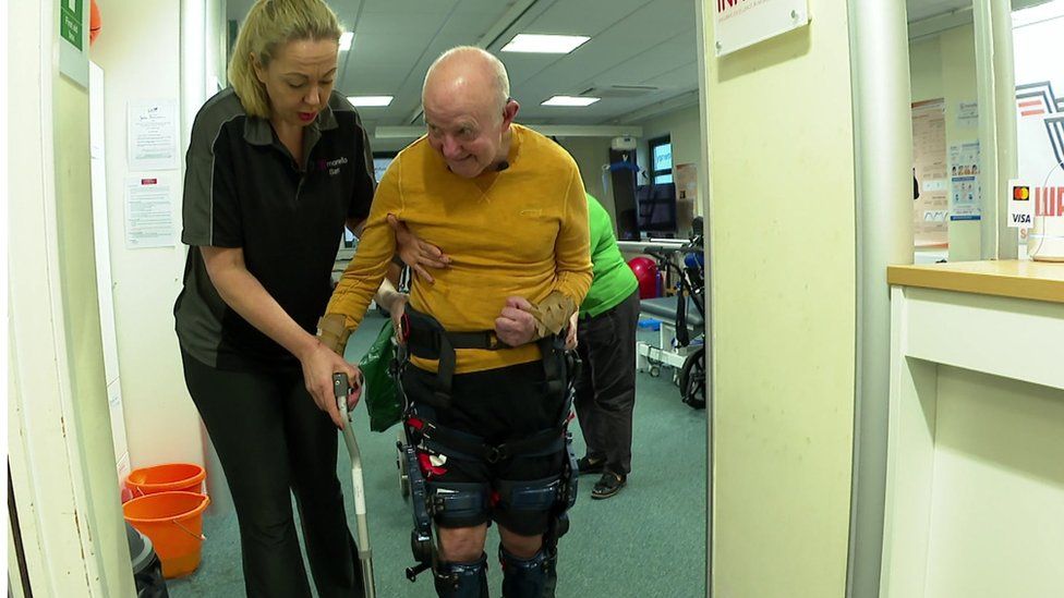 Harold walking in wearable robotic device with a cane