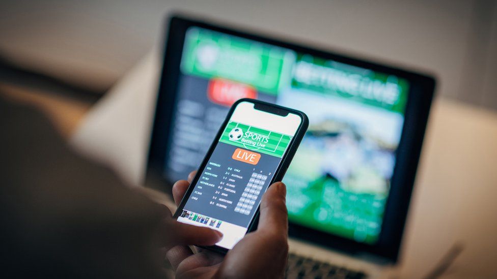 Мужчина использует мобильное приложение для ставок в режиме реального времени и онлайн-азартных игр и смотрит спортивный матч