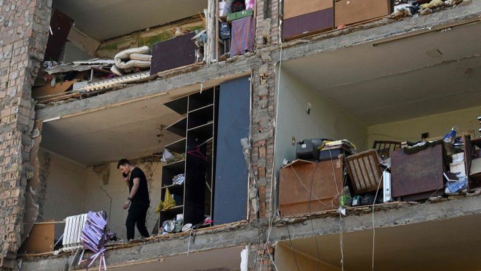 A man talks on his mobile phone in a set of apartments with the exterior wall missing because of Russian shelling