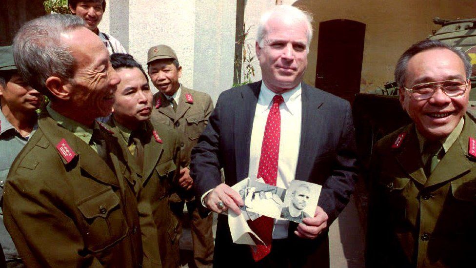 .S. Senator John McCain (C), R-Ariz., a member of the Senate Select Committee on servicemen listed as missing in action (MIA's) in Southeast Asia, holds up photos of himself, as a 30-year-old man wounded and captured in 1967 in North Vietnam, outside the Army Museum in Hanoi 19 October, 1992.