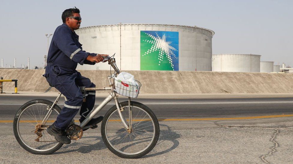A worker rides a bicycle by oil tanks at an oil processing facility of Saudi Aramco.