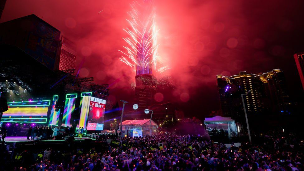 Люди празднуют Новый год в Тайбэе, на Тайване, когда фейерверки освещают небо над зданием Taipei 101