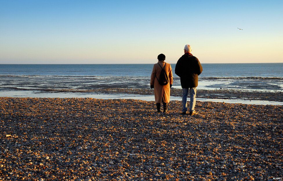 Two elderly people walk on a beach