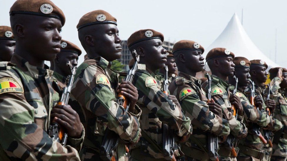 Malian soldiers stand holding rifles and listening to their national anthem during celebrations to mark the country's independence