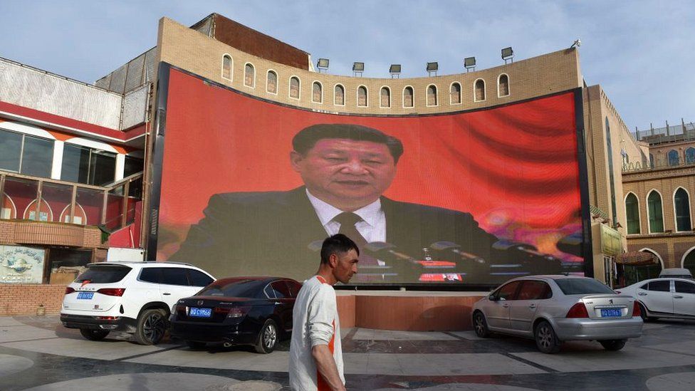 A man walking past a screen showing images of China's President Xi Jinping in Kashgar in China's northwest Xinjiang region