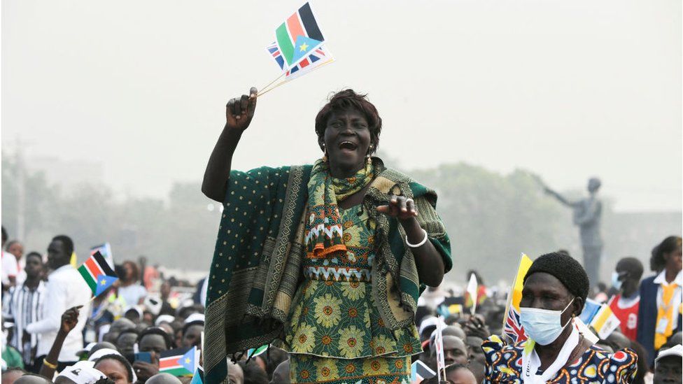 Woman holding South Sudan flag cheering amongst a crowd