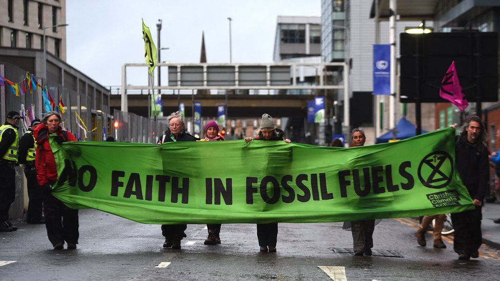 Протестующие маршируют мимо места проведения конференции за большим баннером с призывом против использования ископаемого топлива во время демонстрации изменения климата перед Конференцией по изменению климата COP26 в Глазго 12 ноября 2021 года.