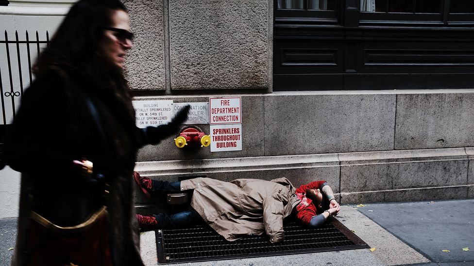 A woman walks past a homeless man in New York