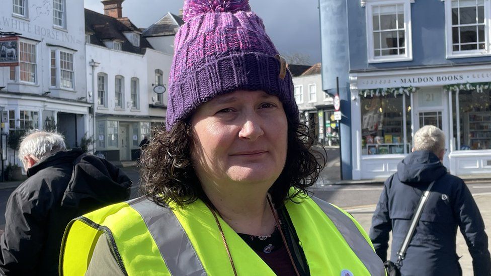 Woman with yellow hi-viz and purple woolly hat standing in a street