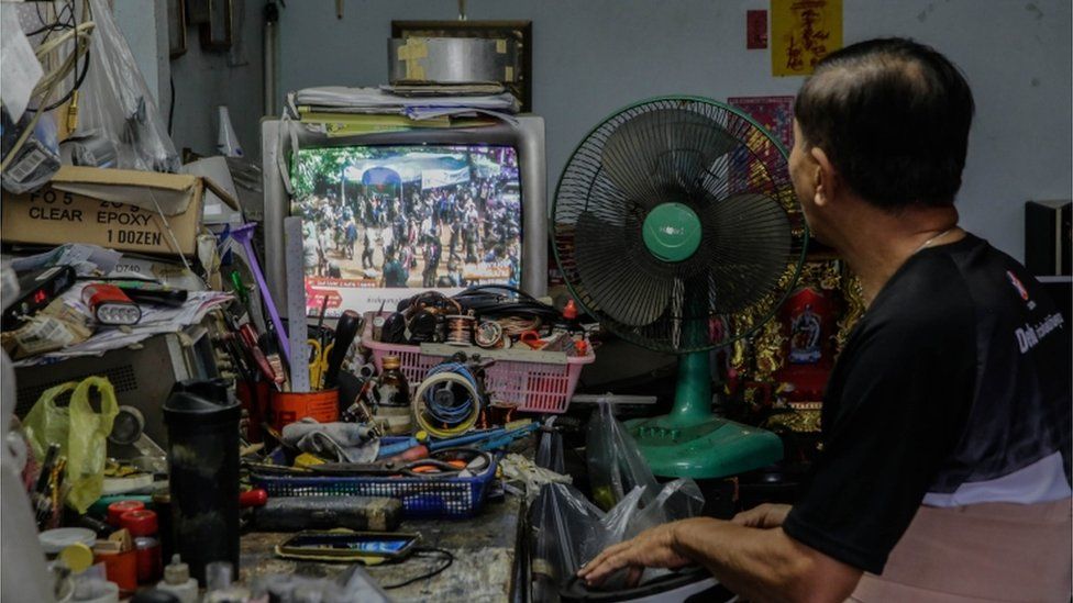 A man is pictured watching the news of the boys' rescue on a television in nearby Chiang Rai