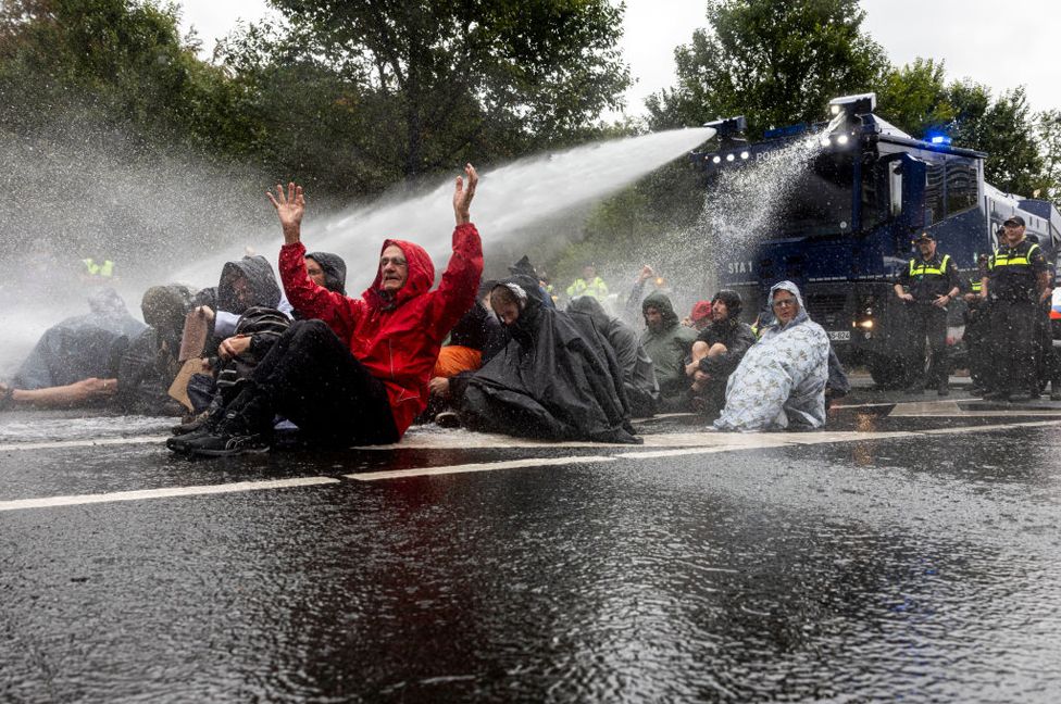 Protesters are sprayed by a police water cannon whilst blocking the A12 Motorway, the main road leading to The Hague, during a climate activist protest on September 20, 2023 in The Hague, Netherlands.