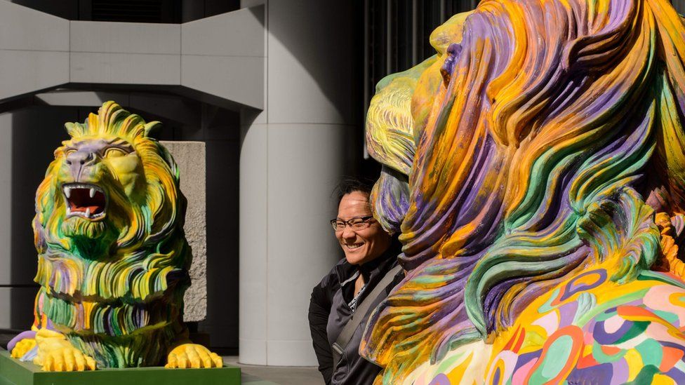 A woman poses between a pair of lions painted in rainbow stripes displayed outside HSBC"s main office in Hong Kong on December 6, 2016