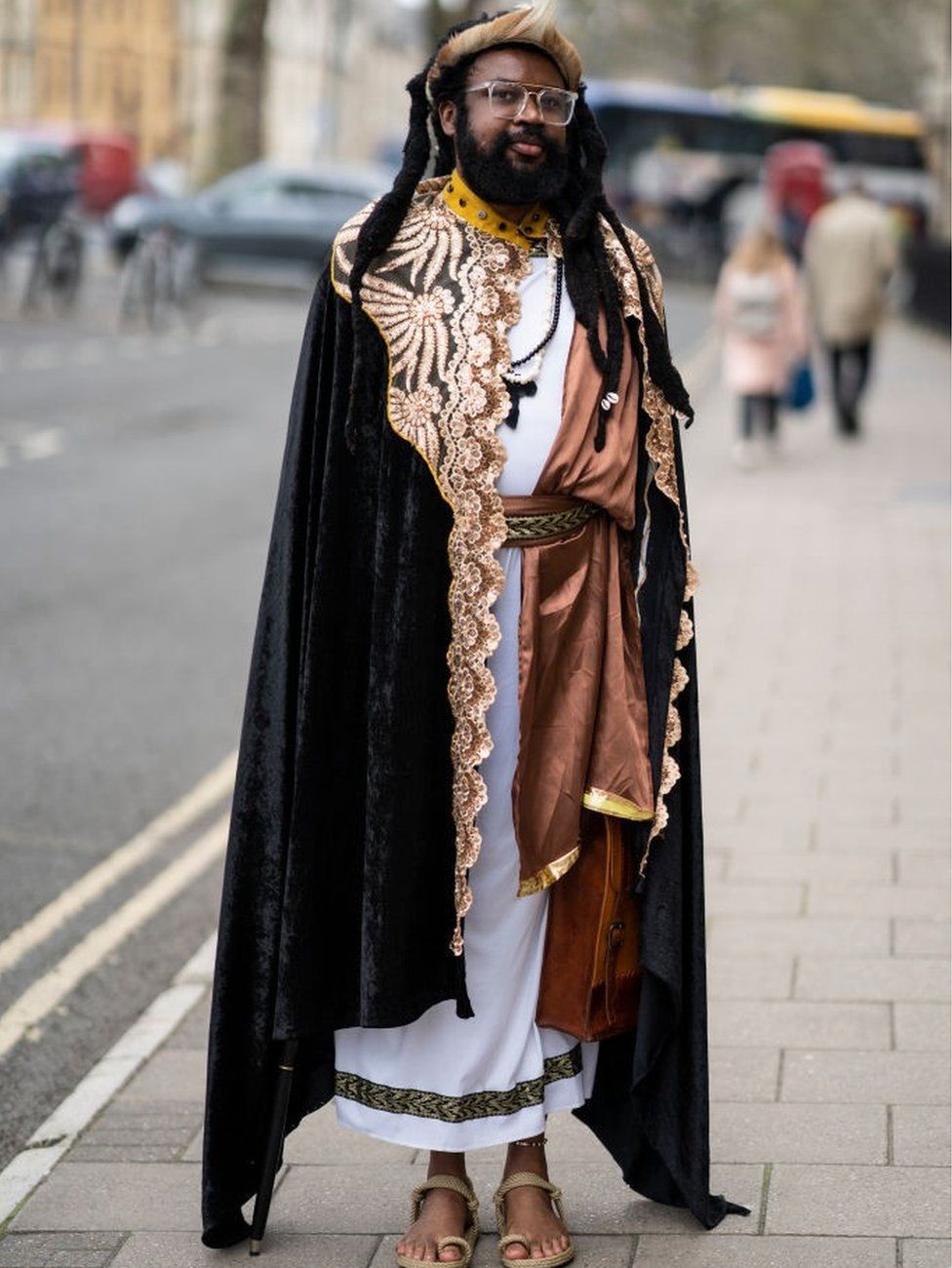 The Nigerian filmaker Onyeka Nwelue, posing for a photo on the street. He is wearing elaborate robes and sandals.