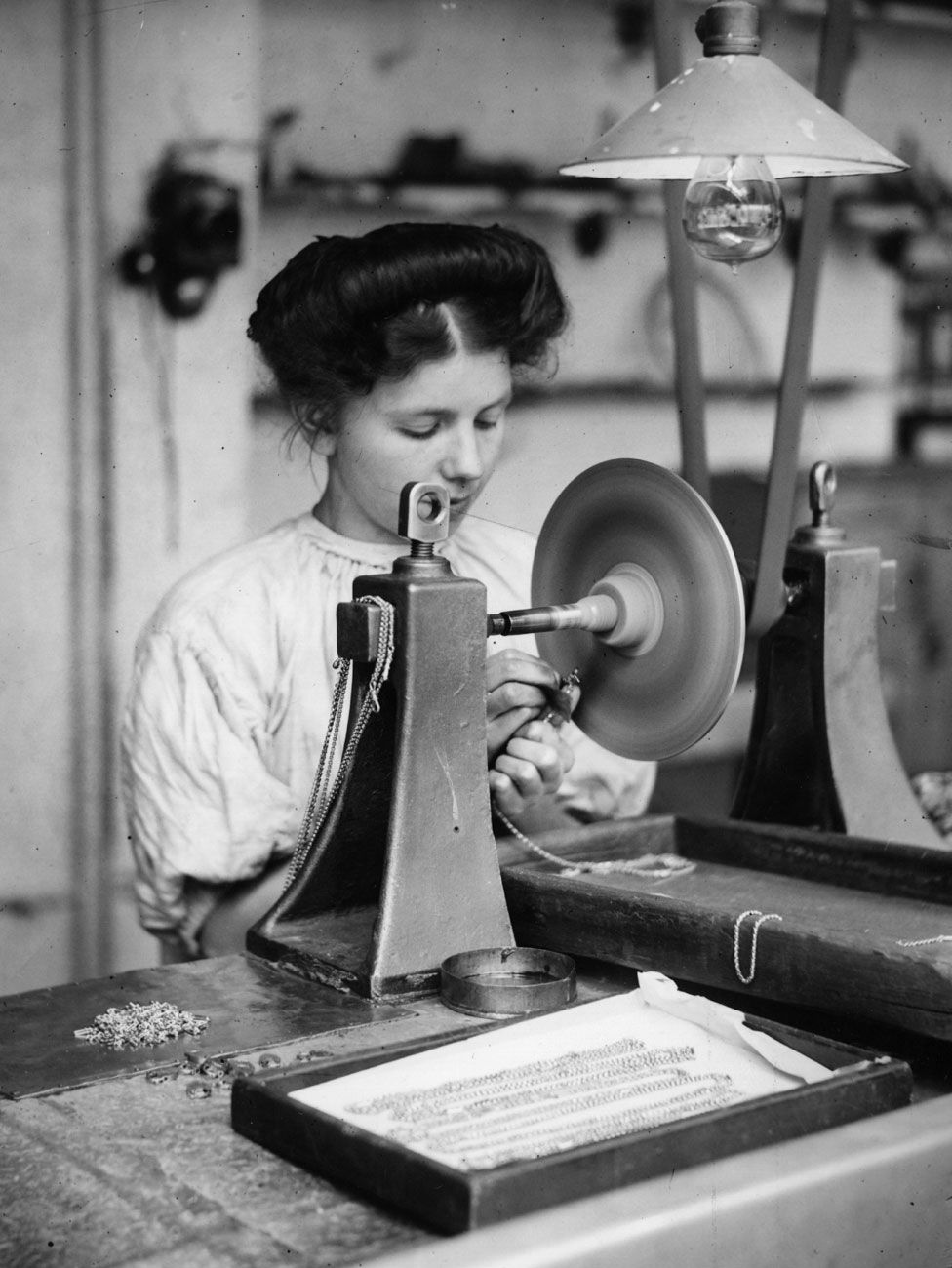 A factory girl works on the finishing of a length of gold chain in 1909