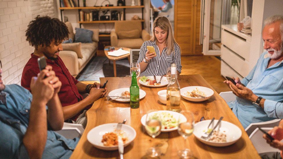 Family sitting around the dinner table on their phones