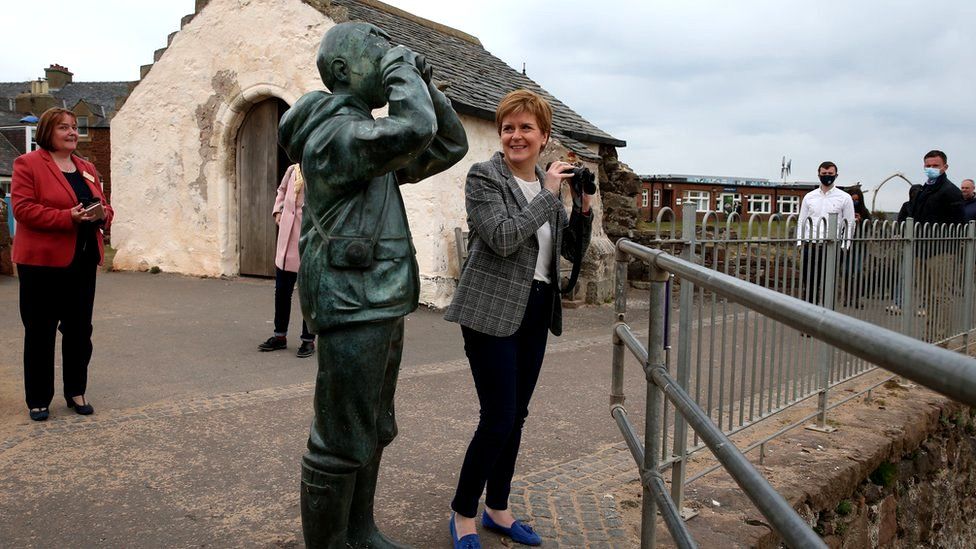 Nicola Sturgeon looks at sculpture holding binoculars, while holding her own binoculars in North Berwick