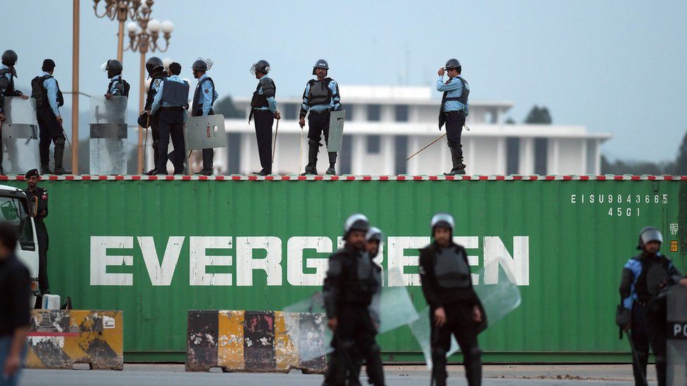 Pakistani policemen stand on the top of a shipping container placed on a road to block access for protesters