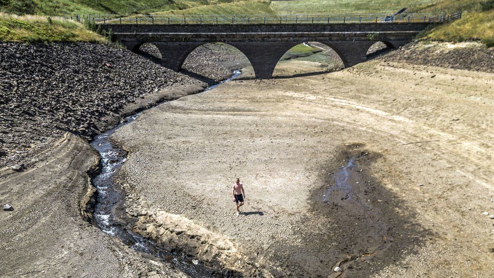 A person walking the dry bed of a tributary to the Dowry Reservoir near Oldham in July