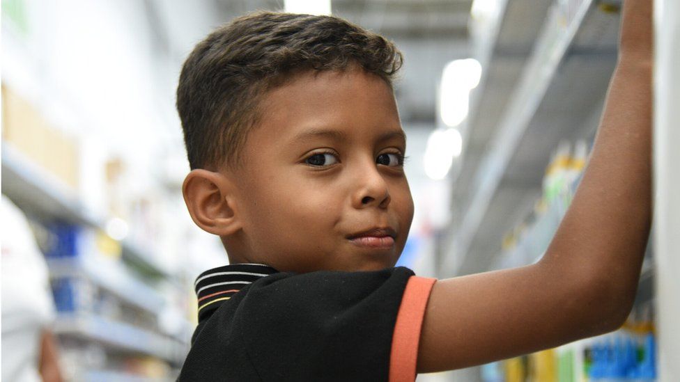 Eight-year-old Derek is buying pens and books with his mother in a shop in San Pedro Sula, as he prepares to restart following a period where he was not able to attend school