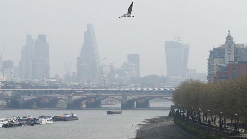 A seagull flies through smog above the skyline of the City of London on April 2, 2014.
