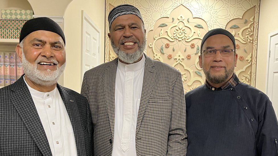 Three men of Bangladeshi heritage stand inside a mosque.