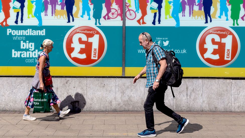 People carrying shopping bags make their way past a window advertisement for Poundland