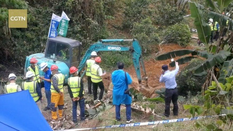 Workers stand around a flooded ditch in the forest crash site