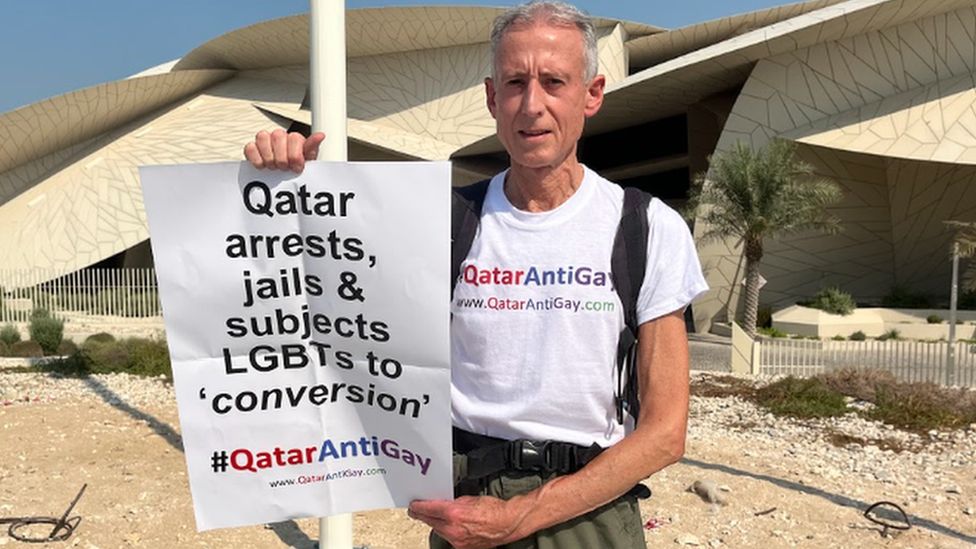 Питер Татчелл держит плакат с хэштегом «Катар против геев»