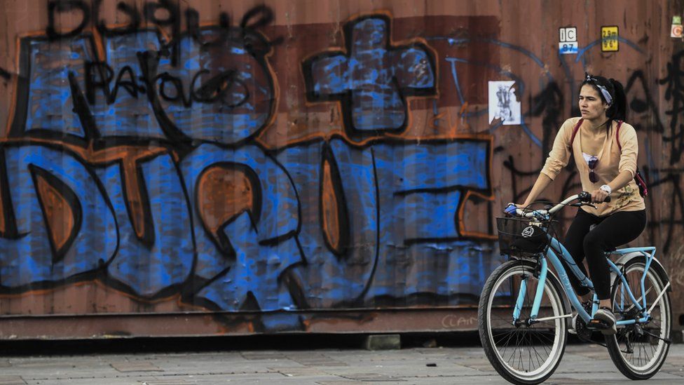 A woman rides her bike by a graffiti against Colombian President Ivan Duque, in Bogota on November 24, 2019.