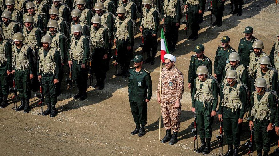 Members of the Islamic Revolutionary Guard Corps (IRGC) attend an IRGC ground forces military drill. One man holds an Iranian flag