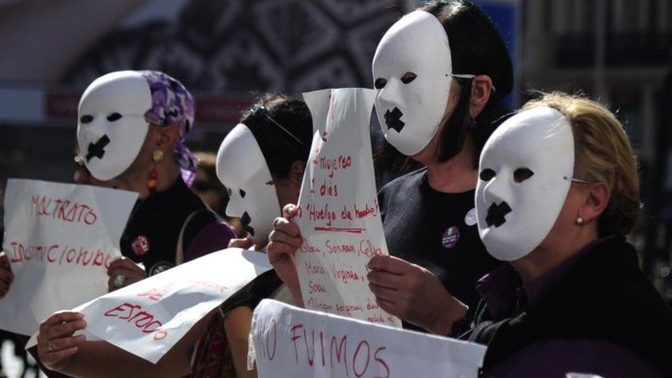 Masked demonstrators in Madrid hold posters against gender violence