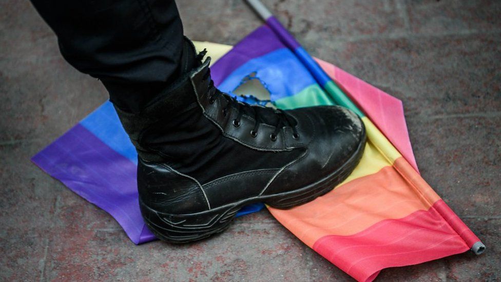 A boot stamping on a ripped rainbow flag
