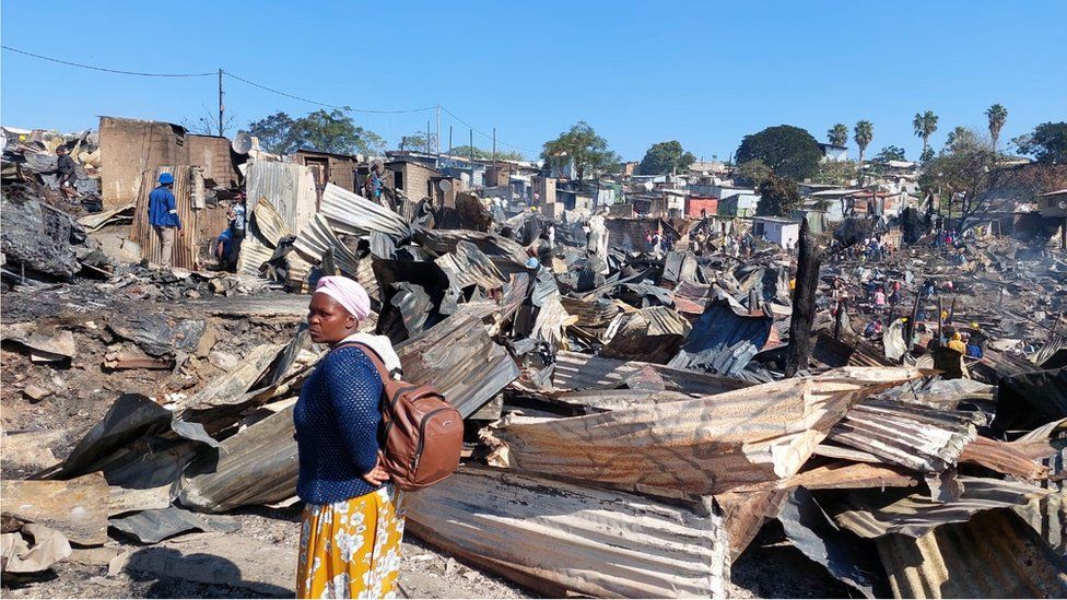 Woman in front of burnt shacks