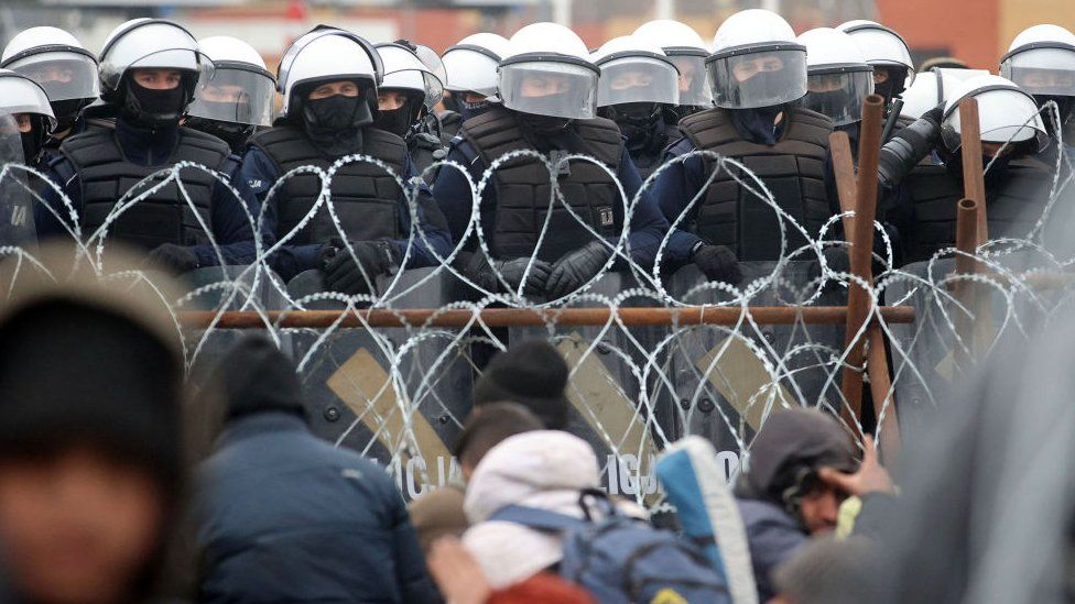 Polish police officers and migrants face each other across barbed wire