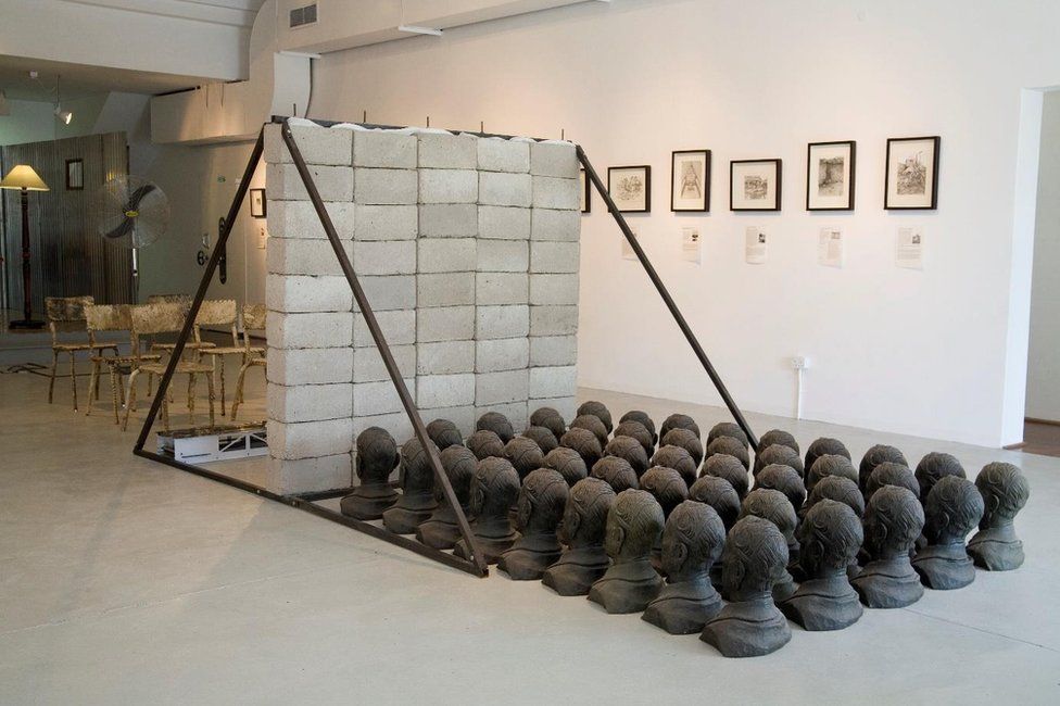 An art installation featuring casts of heads, a brick wall, and chair among other objects