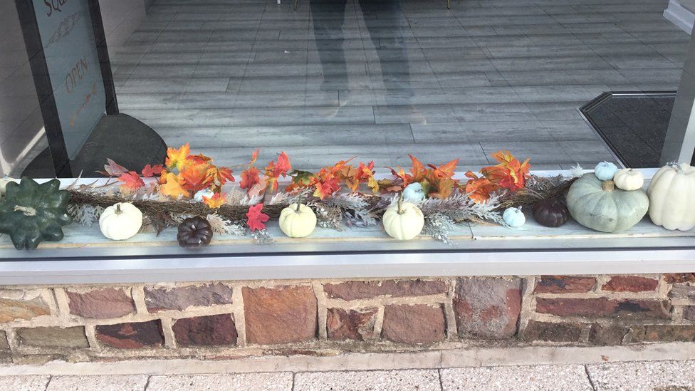 The front of a hairdressers on Hanham high street. There are autumnal leaf decorations and varieties of pumpkins in the window.