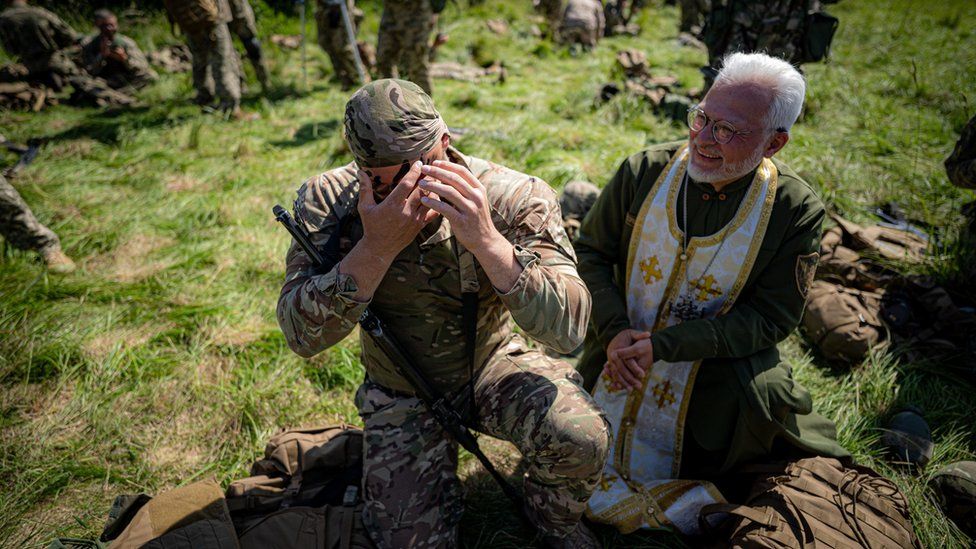 Ukrainian military chaplain 2nd Lieutenant Genadij Rohmanijko, watches a Ukrainian soldier apply camouflage