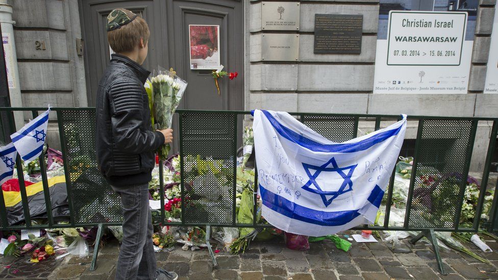 A Jewish boy stands with flowers in front of an Israeli flag and flowers laid in front of the Jewish Museum in Brussels on May 26, 2014,