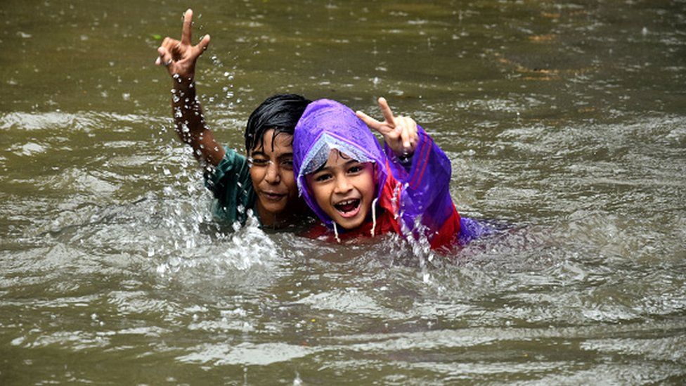 Indian school children play at flooded street during rain showers in Mumbai on July 5, 2022.