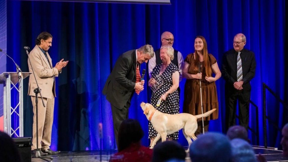 Several people, and a dog, on stage collecting an award