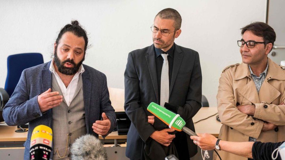 Attorney Patrick Kroker (C) and co-plaintiffs Wassim Mukdad (L) and Hussein Ghrer (R) answer journalists' questions outside the courtroom during a break in a trial against two Syrian defendants accused of state-sponsored torture in Syria, on April 23, 2020 in Koblenz