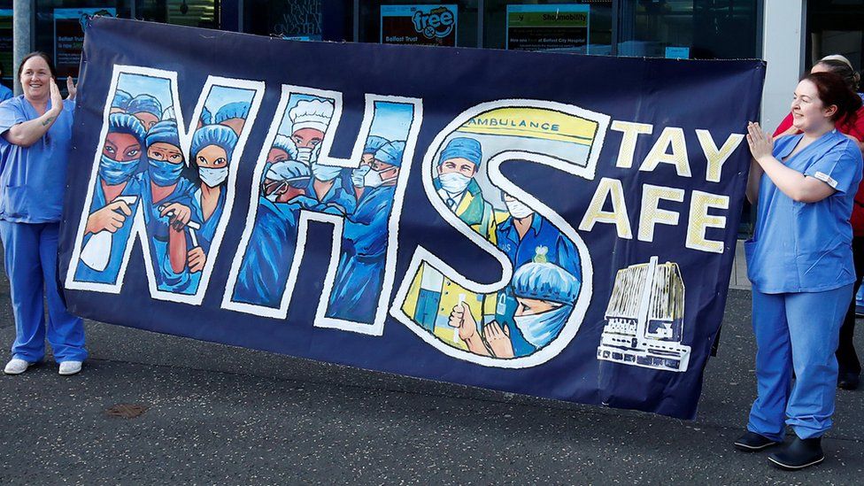 NHS workers at Belfast City Hospital during a Clap for Carers event, in May 2020, hold a banner reading: "NHS stay safe"