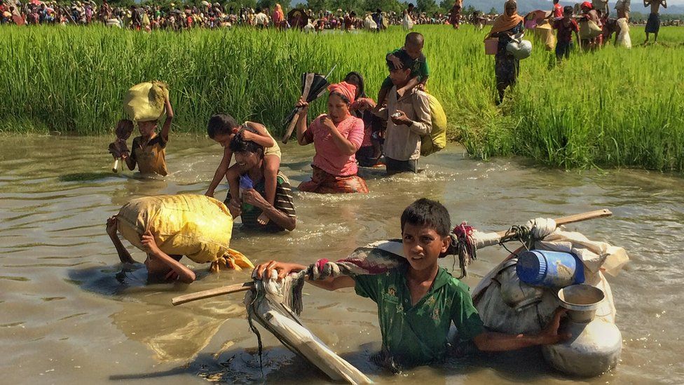 Rohingya children and adults wade through water carrying their possessions