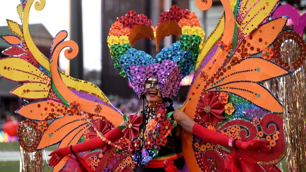 A participant is seen in a huge elaborate rainbow-themed butterfly costume