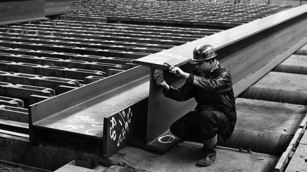 A worker measures a steel girder
