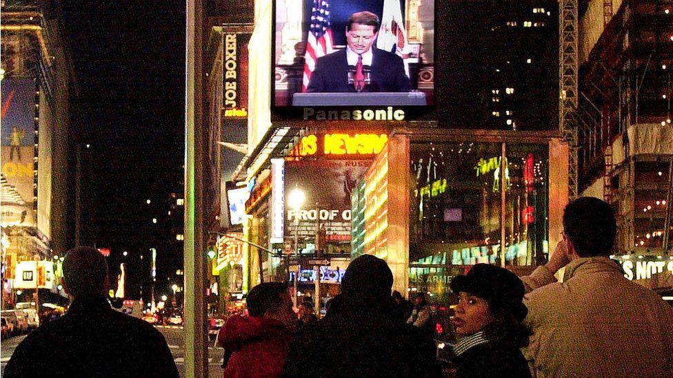 People in Times Square watch Vice President Al Gore concede the race for president to George W. Bush December 13, 2000