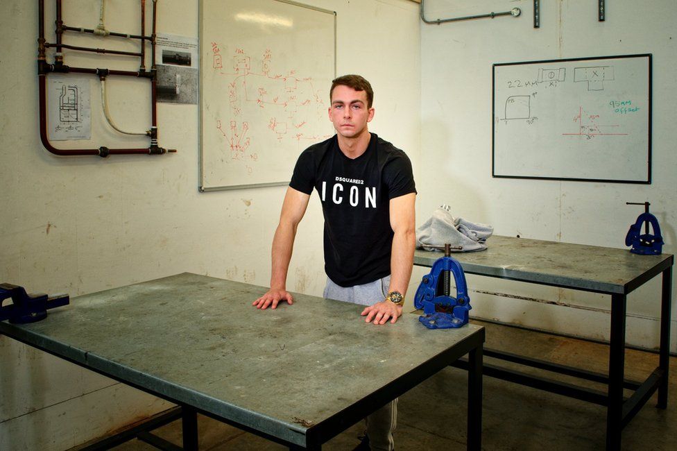 James Claydon inside one of the college workshops where there is an electrical circuit diagram on the wall behind him