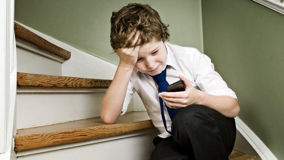 A young boy crying while looking at a smartphone