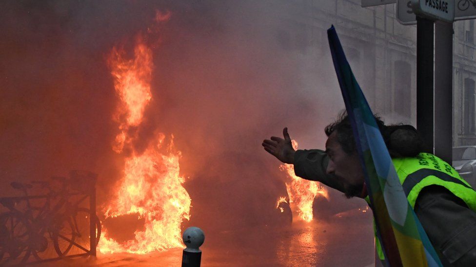 Yellow vest protester gesturing at a burning car