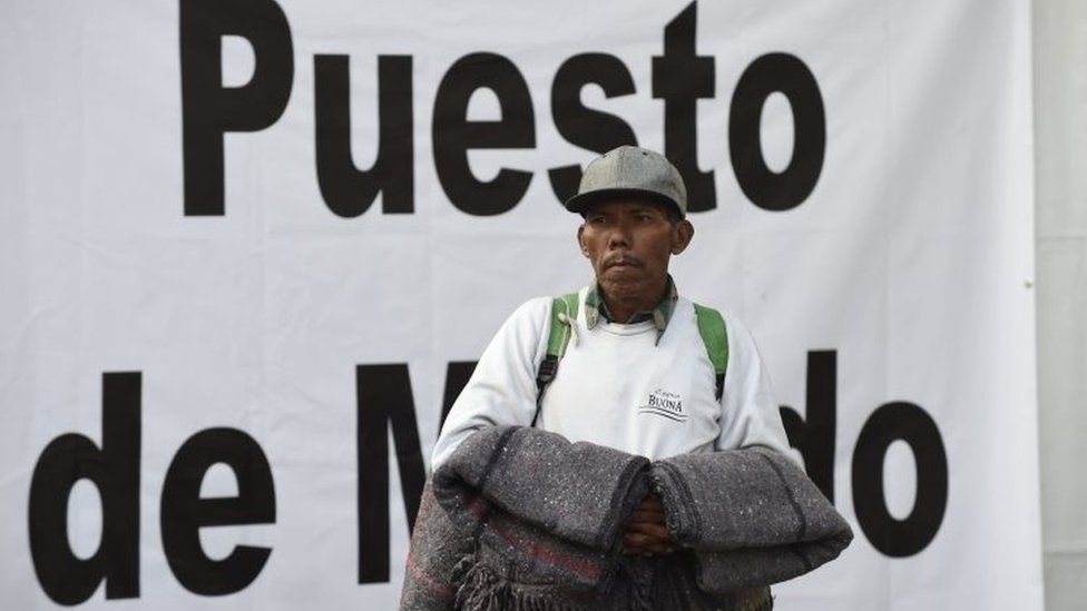 A migrant hold blankets as he looks around the stadium in Mexico City where he has sought shelter